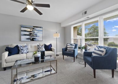 A cozy living room featuring a ceiling fan and stylish blue and white furniture and a glass table with vases